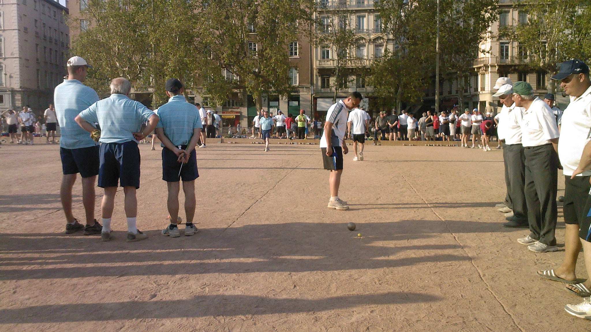 Outdoor pétanque tournament players tossing metal boules on a gravel court