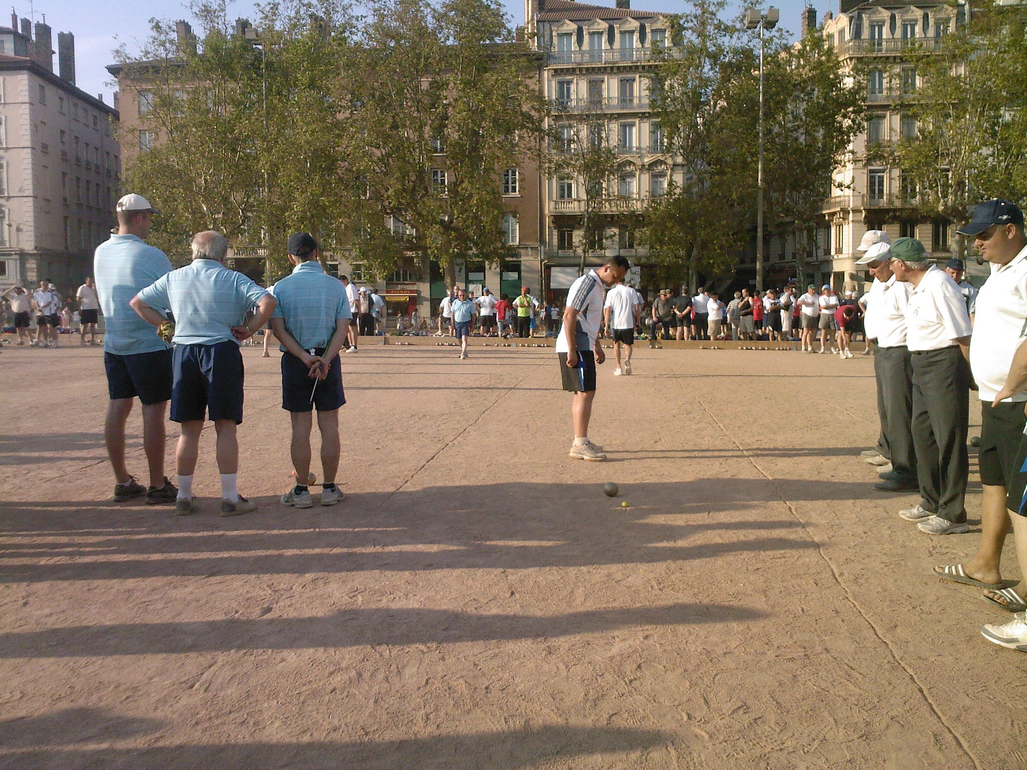 Outdoor pétanque tournament players tossing metal boules on a gravel court